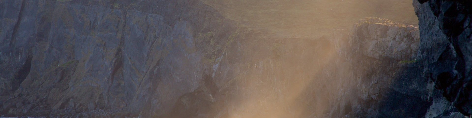 A coastal scene with a rocky cliff, a beach, and a lighthouse in the distance.
