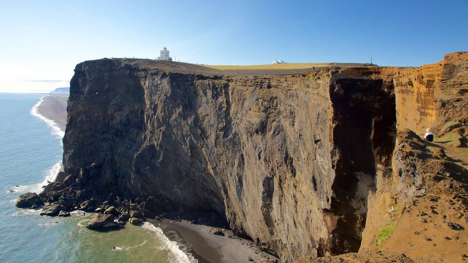 A coastal cliff with a lighthouse, beach, and rocky shoreline.