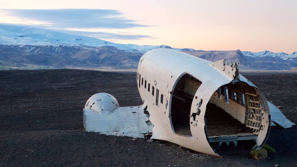 A damaged aircraft in a barren landscape with snow-capped mountains in the background.
