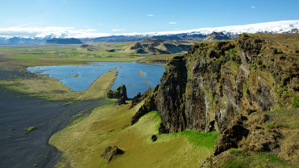 A coastal landscape with cliffs, a river, and distant snow-capped mountains.