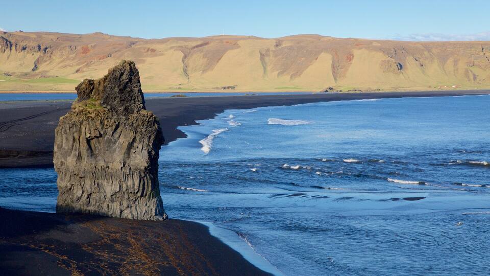 A rocky cliff by a beach with waves crashing against it.