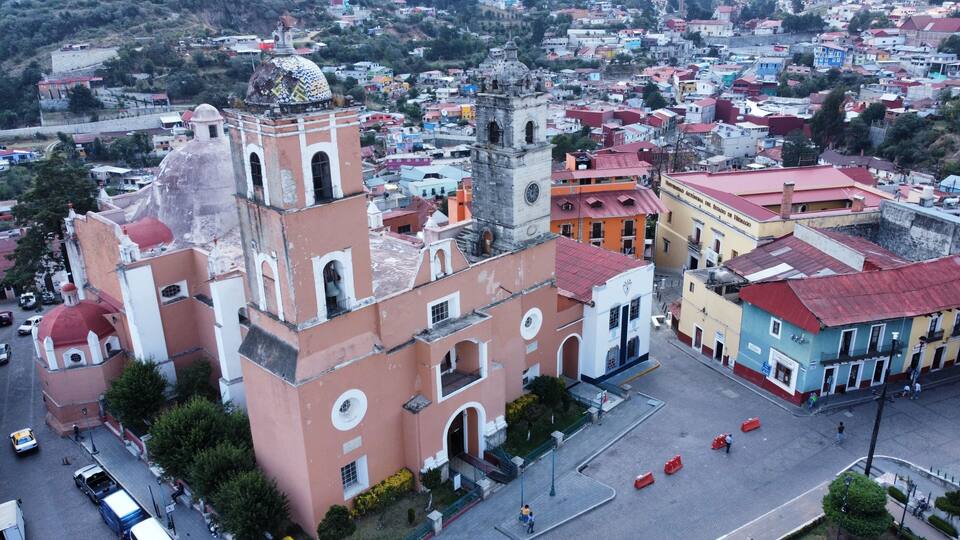 A historic church with a bell tower and a clock, surrounded by colorful buildings and a cobblestone street.