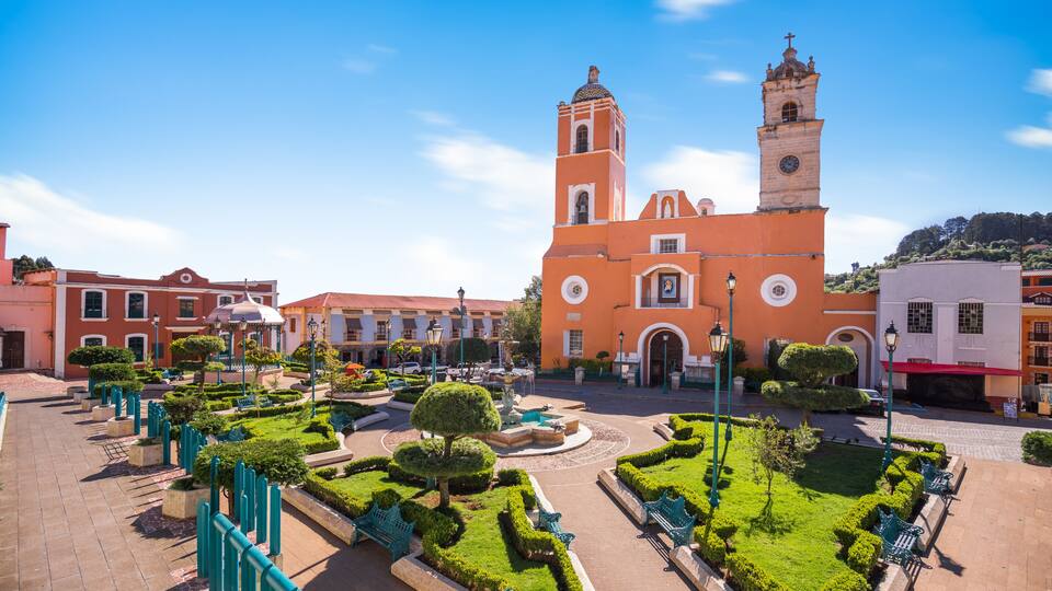 A plaza with a church, benches, and well-maintained gardens.