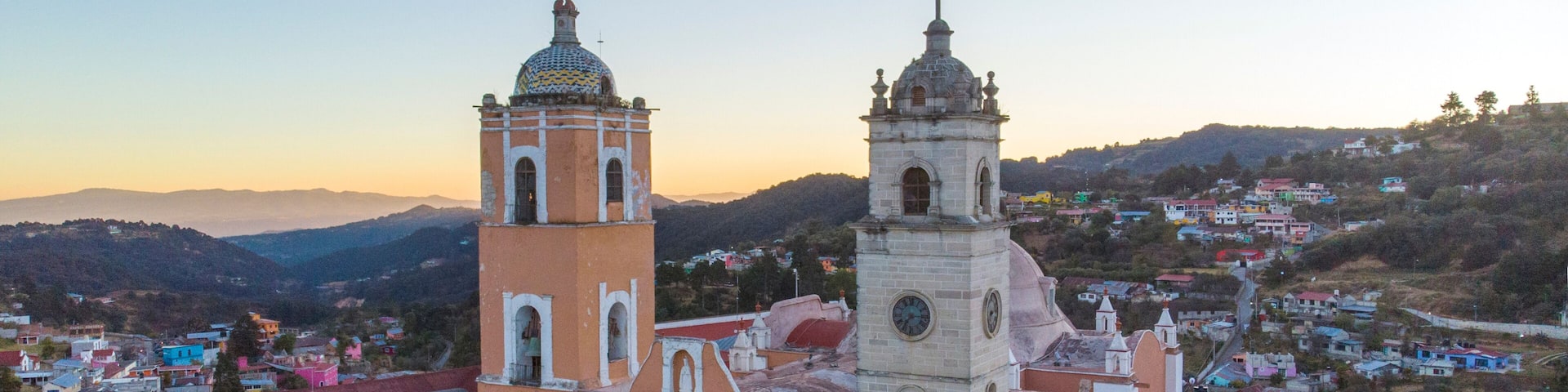 A church with two towers and a dome, surrounded by colorful buildings and a hilly landscape.