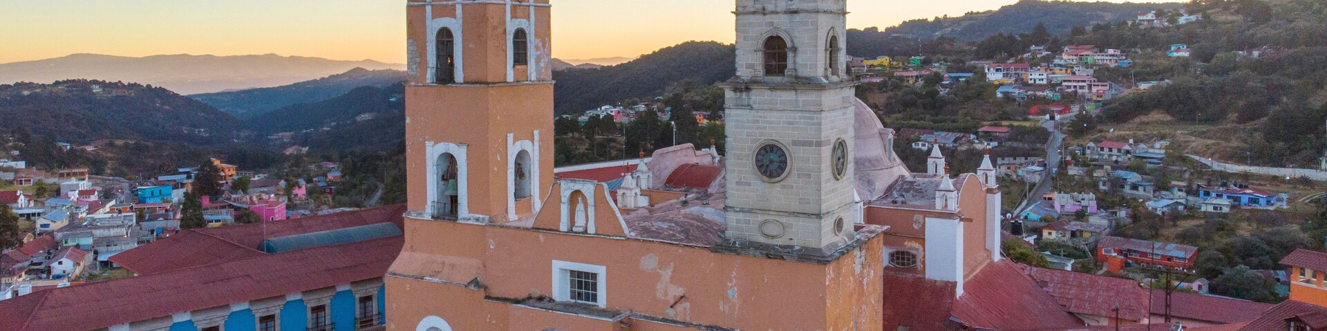 Una iglesia con dos torres y una cúpula, rodeada de edificios coloridos y un paisaje montañoso.