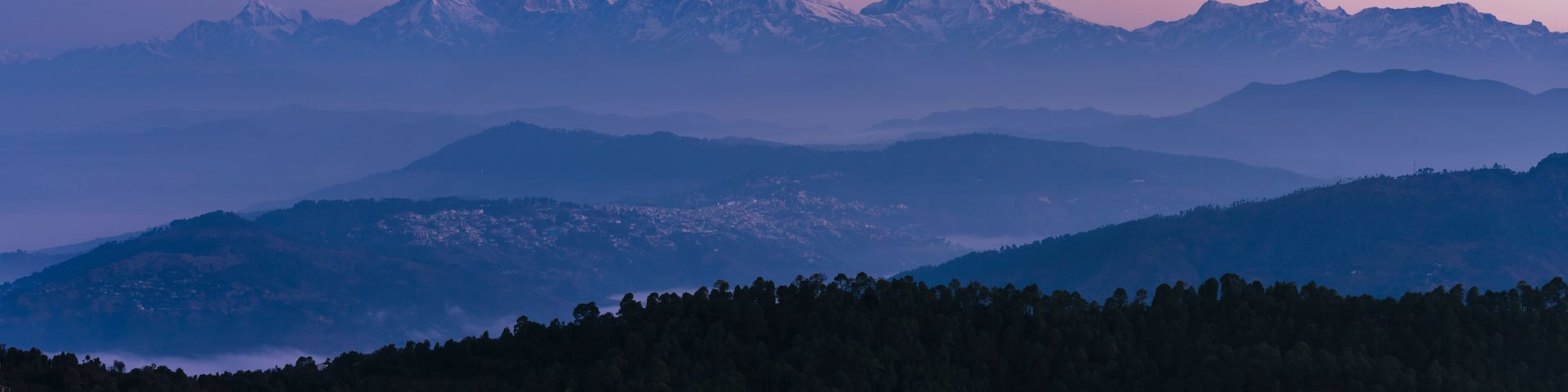 A mountain range with snow-capped peaks and a forested valley.