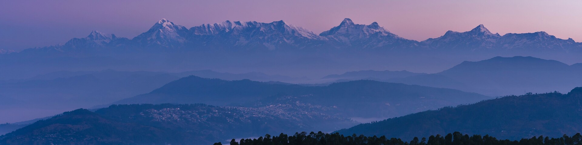 Uma cordilheira com picos nevados e um vale florestado.