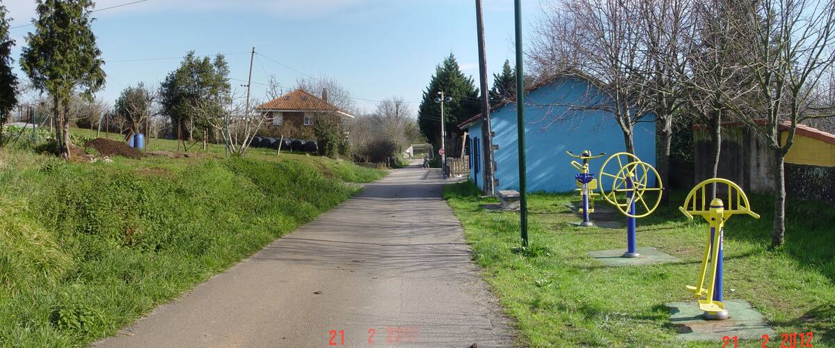 A rural pathway with a blue building, trees, and outdoor exercise equipment.