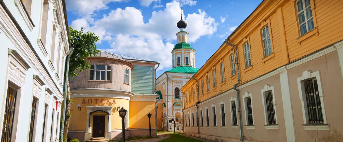 A historic street with buildings, a green lawn, and a church with a green dome.