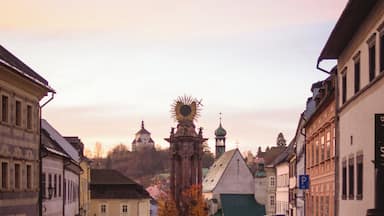A cobblestone street lined with historic buildings, a prominent clock tower, and a church with a green roof.