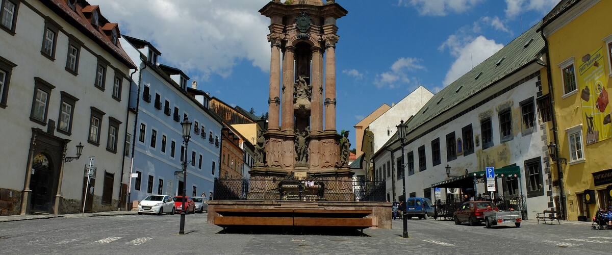 A historic monument with statues, surrounded by old buildings and a clear sky.