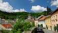 A town with historic buildings, a church with a clock tower, and a car parked on a cobblestone street.