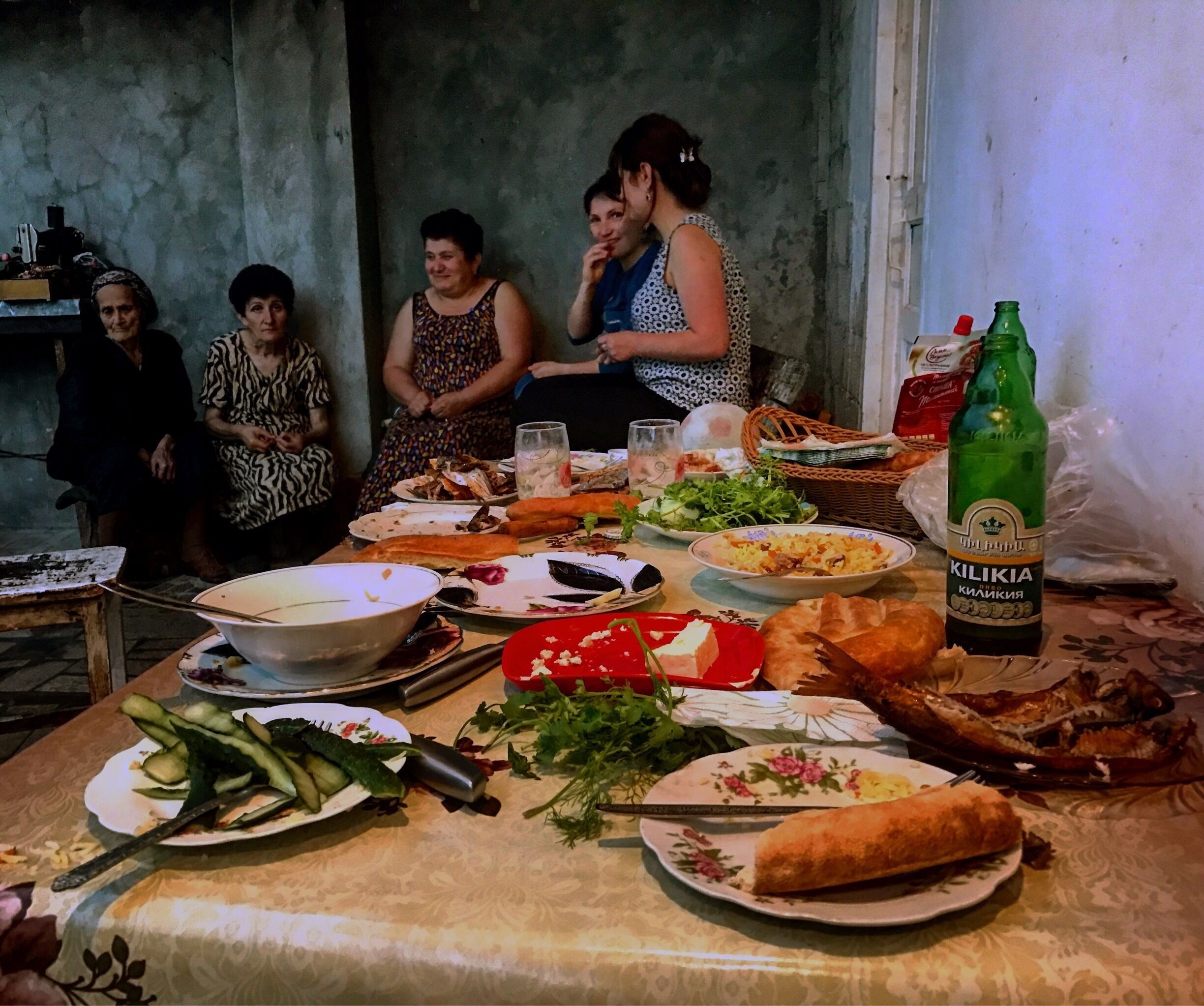 A group of people around a table with various dishes, a bottle of beer, and some vegetables.
