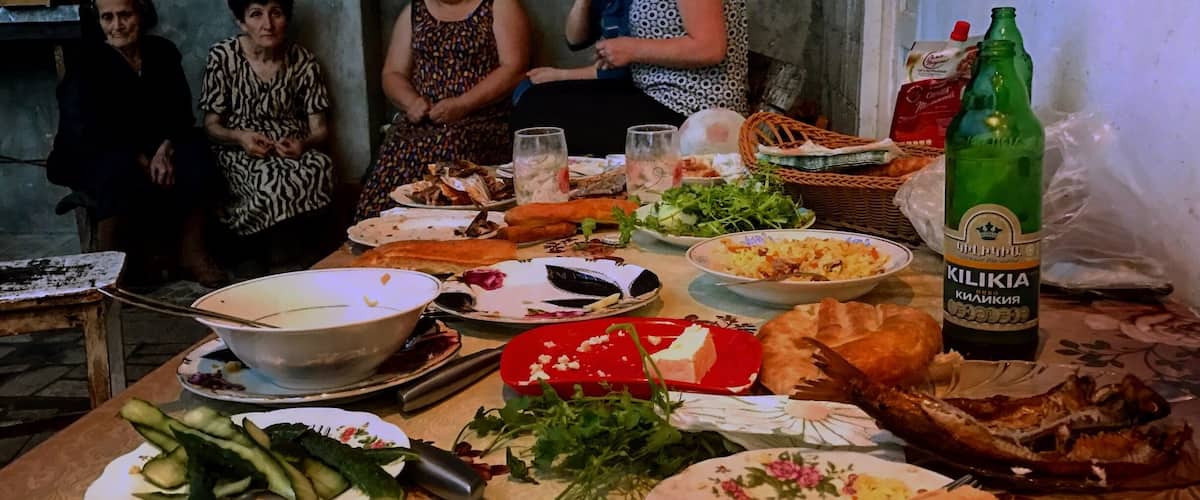 A group of people around a table with various dishes, a bottle of beer, and some vegetables.