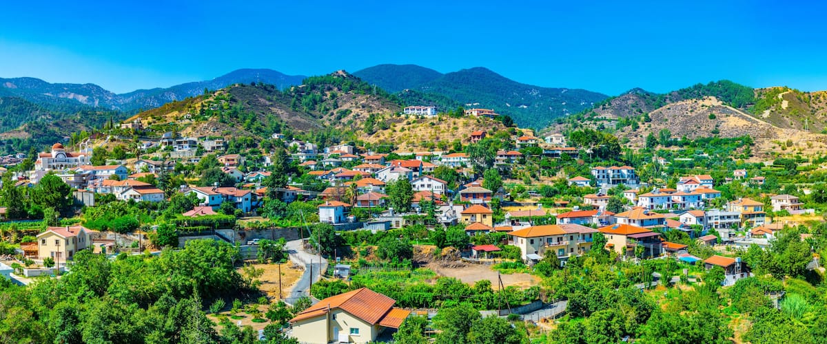 A hillside village with red-roofed houses, lush greenery, and mountains in the background.