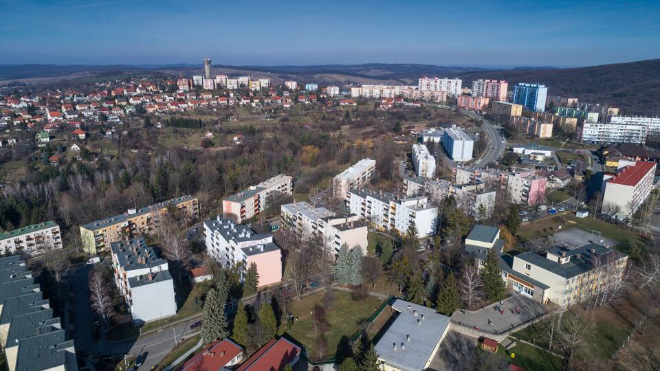 An aerial view of a town with a mix of residential and commercial buildings, surrounded by hills and sparse vegetation.