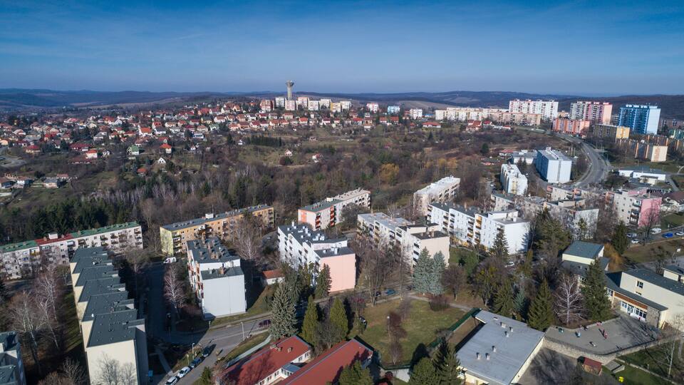 A cityscape with a mix of residential and commercial buildings, a prominent tower, and a hilly backdrop.