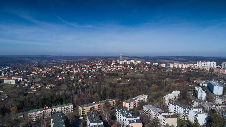 A panoramic view of a city with a prominent tower, residential buildings, and surrounding hills.