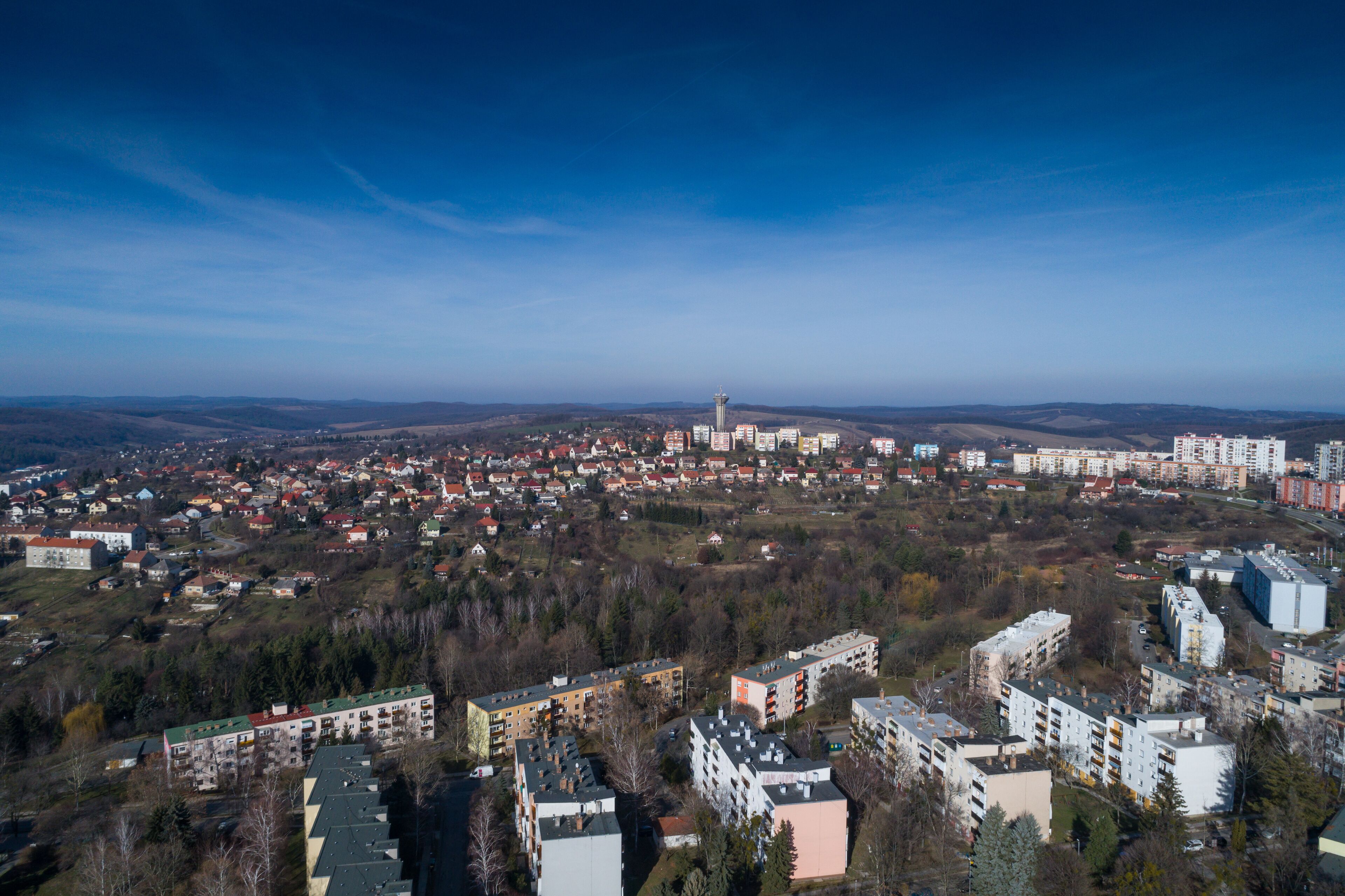 A panoramic view of a city with a prominent tower, residential buildings, and surrounding hills.