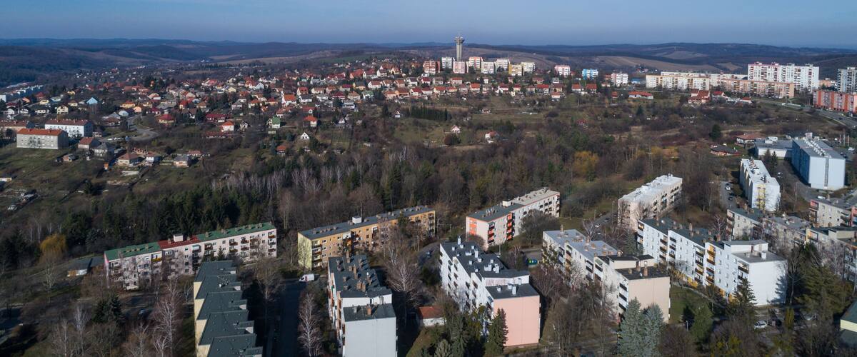 A panoramic view of a city with a prominent tower, residential buildings, and surrounding hills.