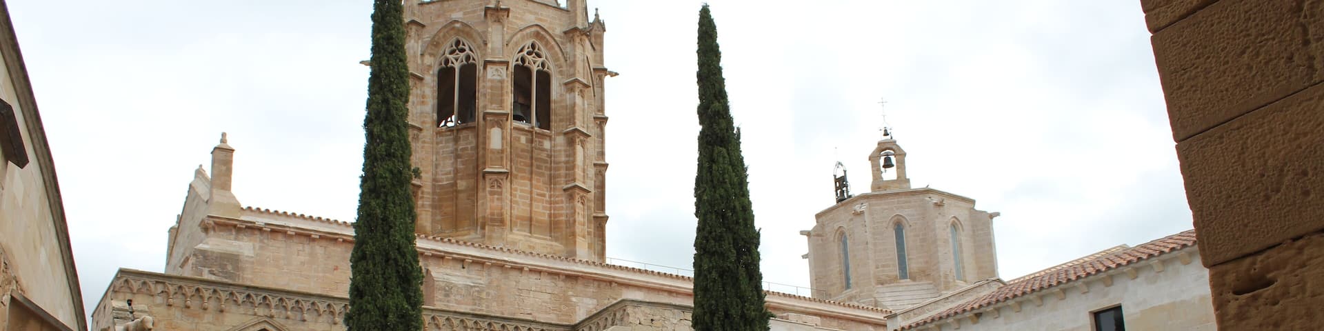 Monastery of Santa Maria de Vallbona The Monastery of Santa Maria de Vallbona (Catalan: Santa Maria de Vallbona de les Monges; Spanish: El Real Monasterio de Santa María de Vallbona) is a Cistercian abbey in Vallbona de les Monges, in the comarca of Urgell, Catalonia, Spain. Founded in the early 12th century, it is one of the most important monasteries in Catalonia; its church represents an example of transition between Romanesque and Gothic architecture. The abbey was declared a national monument in 1931. Initially the monastery consisted in a community of hermits, documented from 1157, which followed the Benedictine rule; in 1175, however, only a small group of nuns remained. In 1163 they had received territories from Ramon Berenguer IV, count of Barcelona, and in that year decided to switch to the Cistercian order. Two years later the abbey received several privileges from King Alfonso I of Aragon, and subsequently it could expand thanks to the numerous donations from noble families. The cloister is on a quadrangular plan, whose sides, of different lengths, correspond to different, successive ages and construction styles (12th-15th centuries). The oldest sector, on the south, shows the original, sober Romanesque-Cistercian canons: it has three spans formed by three piers, with three rounded arcades supported by columns with undecorated capitals. The eastern wing is also in Romanesque style (early 13th century), and has five spans divided by four pilasters, The arcades form triple mullioned windows with, in the mullions, small rose windows with decoration in Arabic style. The capitals of the columns have vegetable motifs. The northern wing is the shortest one; it has wide hollows with ogival traceries in Gothic style, dating to the 14th century. The western side, the most recent one, was built in the 15th century in proto-Renaissance style. The capitals of the columns show the heraldic symbols of the Caldés family, who produced the monastery's abbesses during that period. The Capitular Hall is accessed from the cloister through a Gothic gate built under abbess Anglesola in the 14th century, and has a cross-vault cover. The pavement features several tomb slabs of abbesses, and there is an alabaster image of the Virgin of Mercy, attributed to the sculptor Pere Johan. (source: en.wikipedia.org/wiki/Monastery_of_Santa_Maria_de_Vallbona)