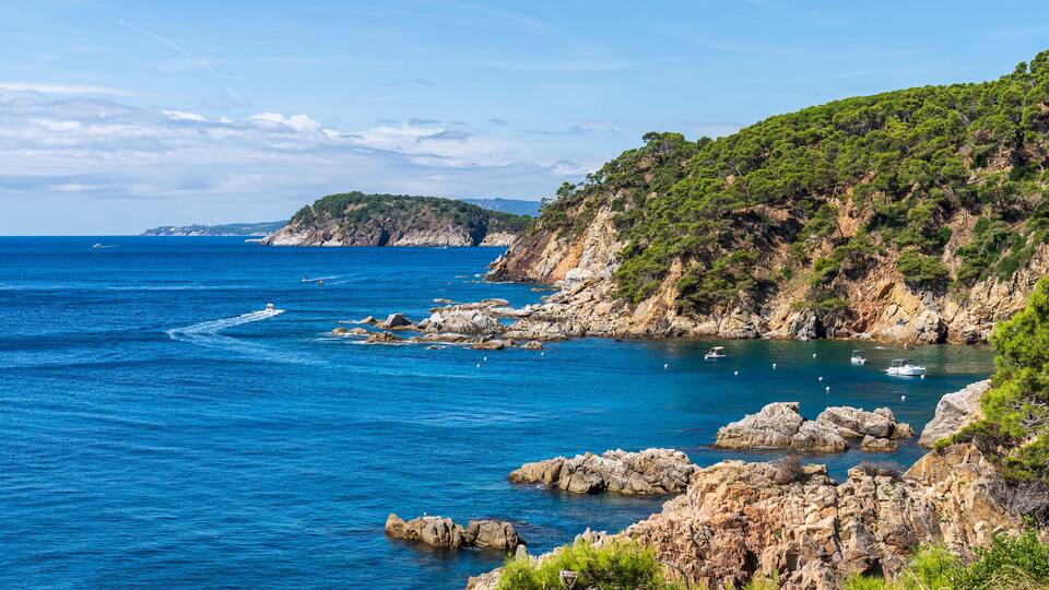A coastal landscape with rocky cliffs, clear blue sea, and distant land.