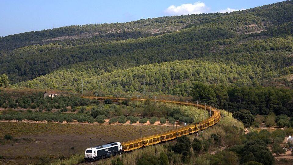 A train traveling on a curved track through a hilly, forested area.