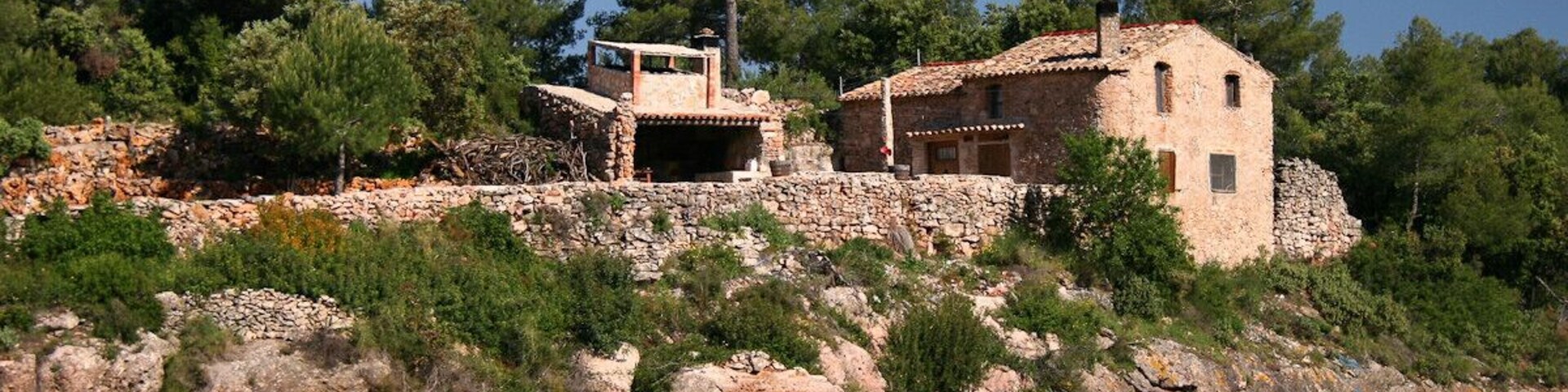 A stone house on a hillside with vineyards in the foreground.