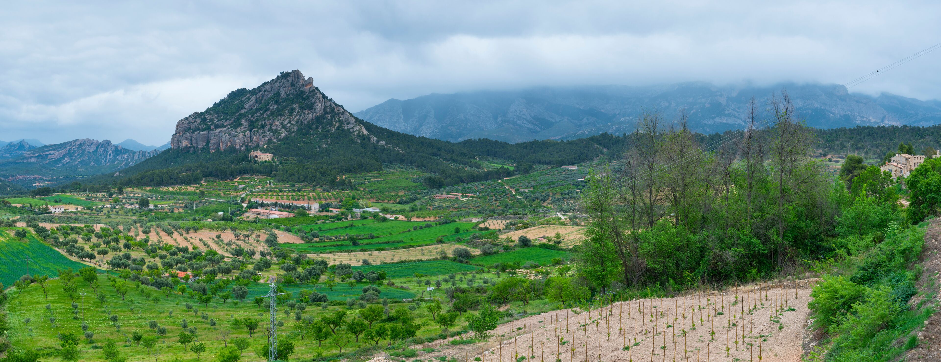 A mountainous landscape with terraced fields, a prominent rocky peak, and scattered buildings.