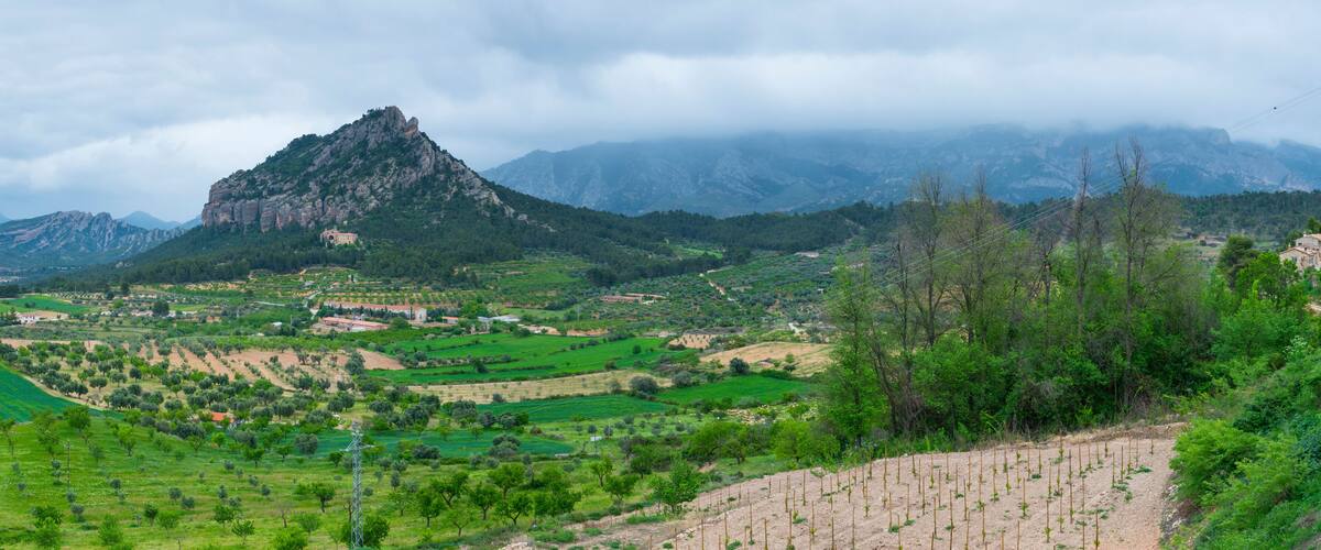 A mountainous landscape with terraced fields, a prominent rocky peak, and scattered buildings.