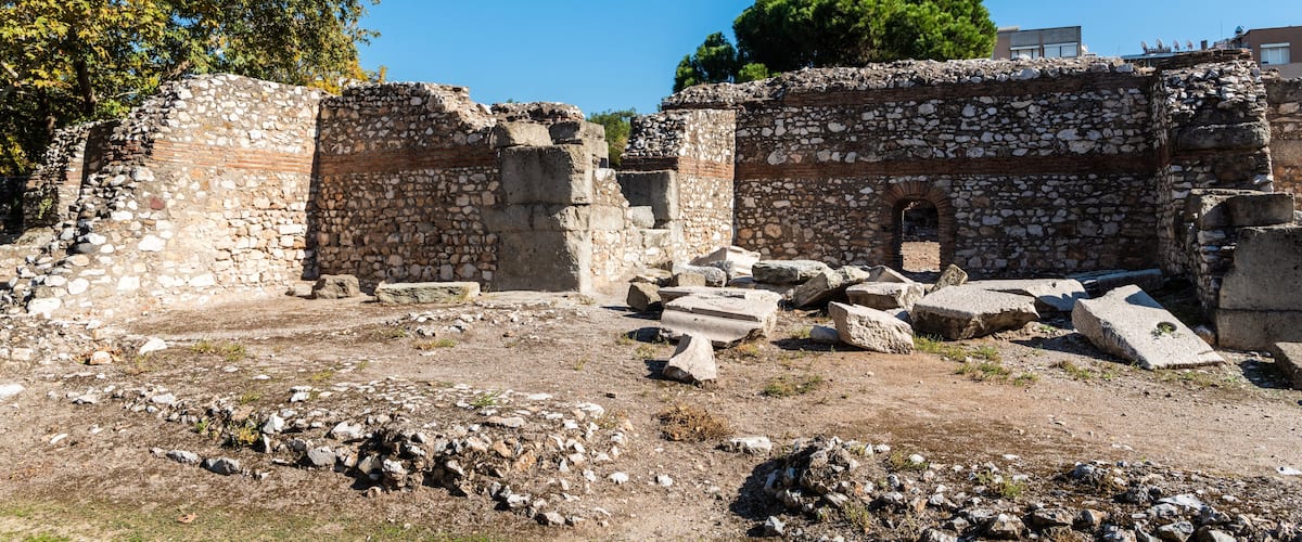 Ancient stone ruins with scattered debris, a large tree, and a clear blue sky.