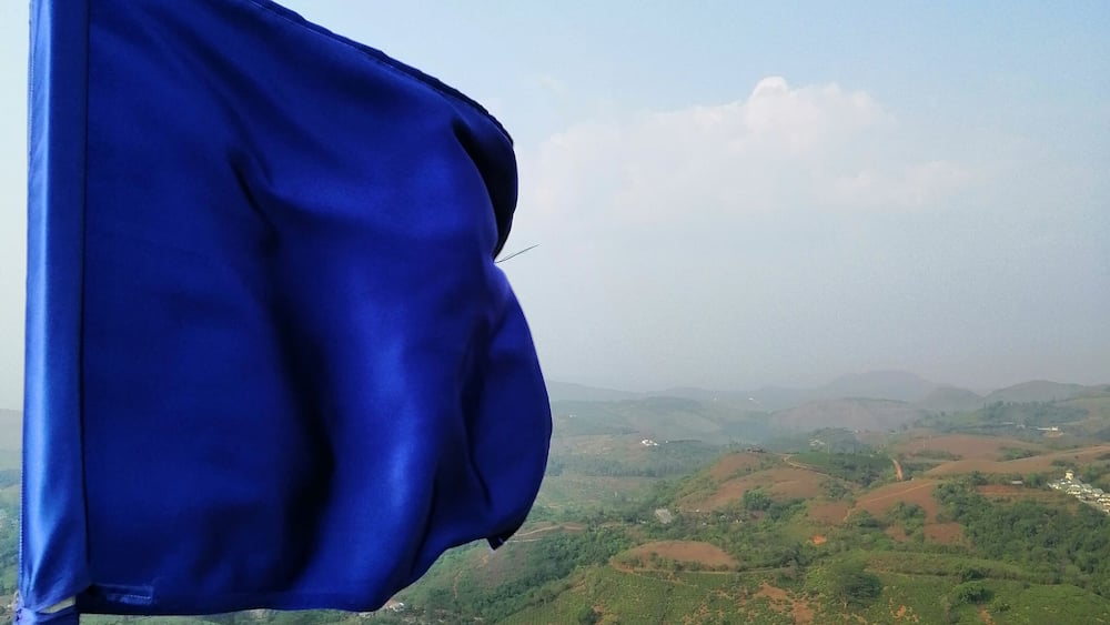 A blue flag on a pole with a view of a hilly landscape in the background.