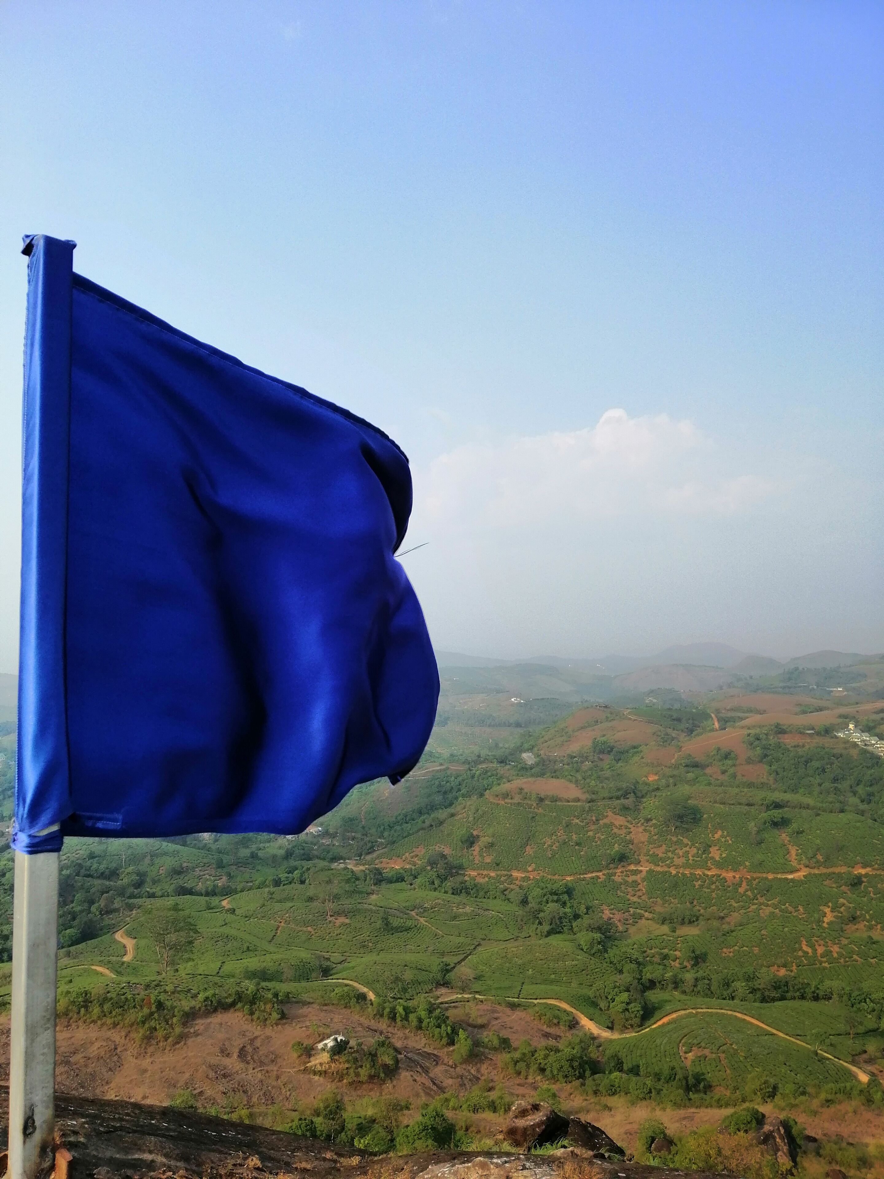 A blue flag on a pole with a view of a hilly landscape in the background.