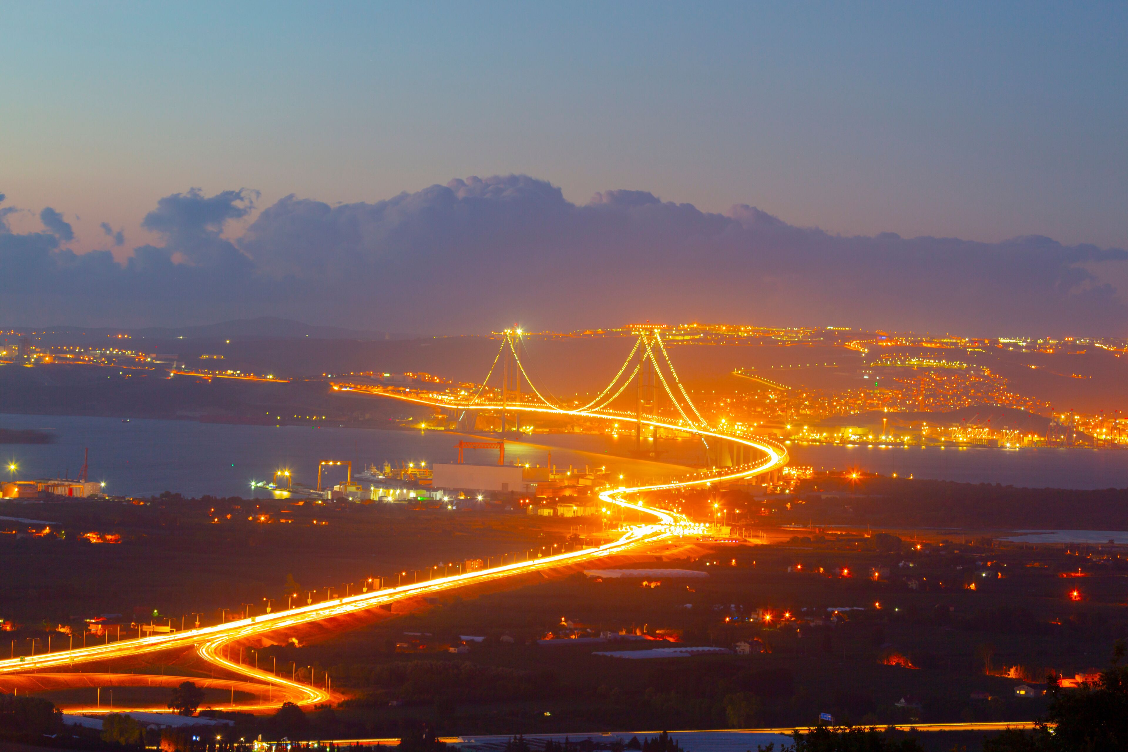 A cityscape at dusk with illuminated highways and a prominent bridge structure.