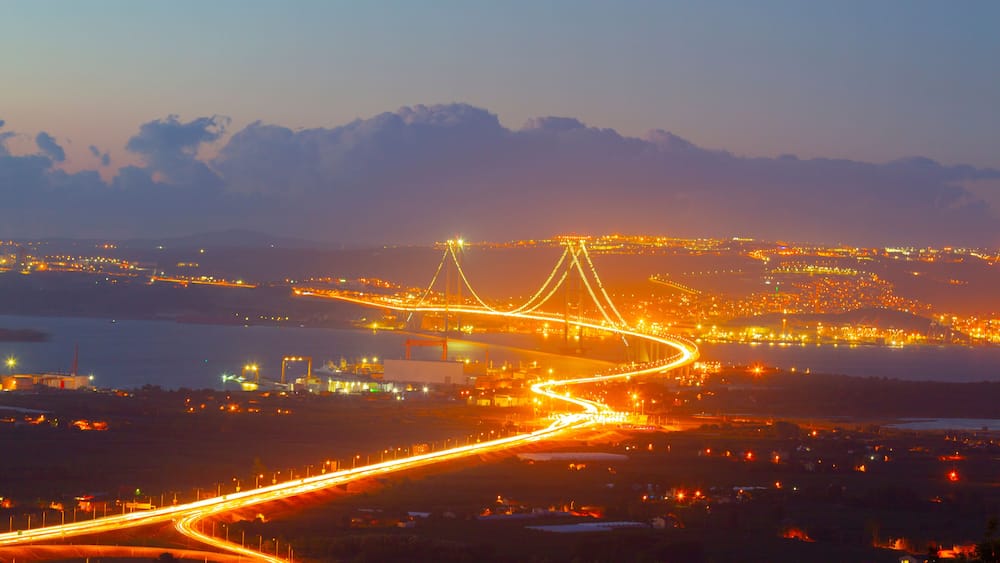 Une vue d’une ville au crépuscule, avec des autoroutes illuminées et un pont imposant.