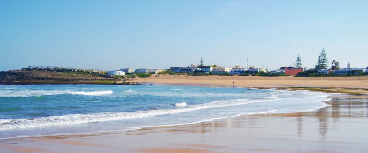 A beach with waves, a sandy shore, and buildings in the background.