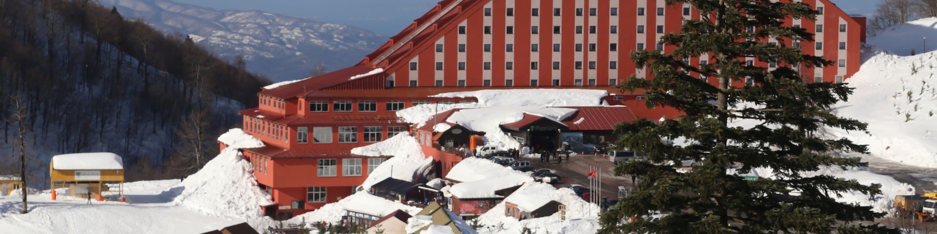 A large red building with a steep roof, surrounded by snow-covered ground and trees.