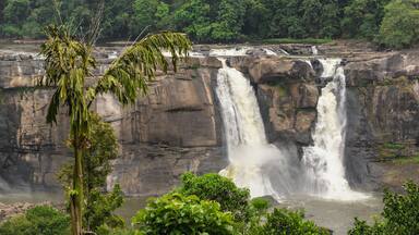 A multi-tiered waterfall cascading over rocky cliffs surrounded by dense greenery.