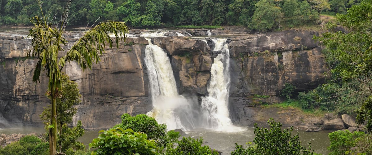 A multi-tiered waterfall cascading over rocky cliffs surrounded by dense greenery.