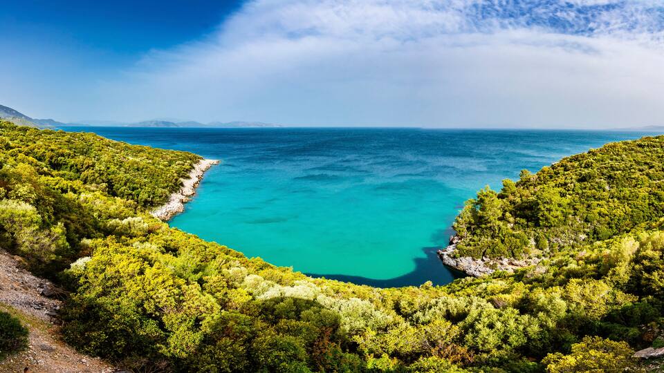 A turquoise sea surrounded by dense green forest and rocky coastline.