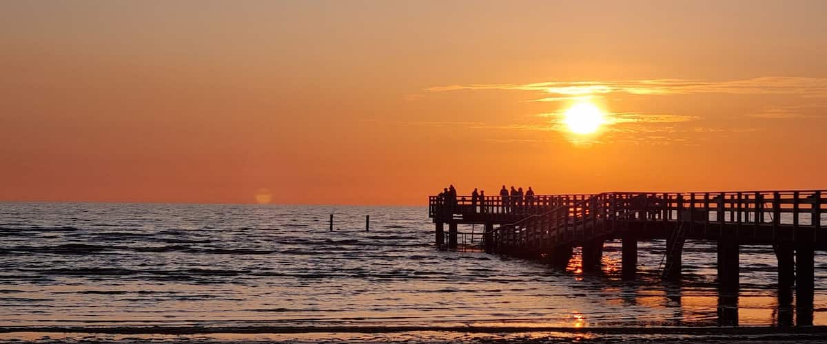 A sunset over the ocean with a pier extending into the water.