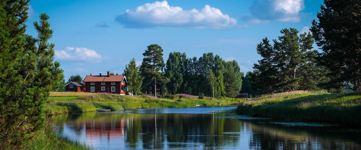 A calm river with a boat, a red house, and a forested area.