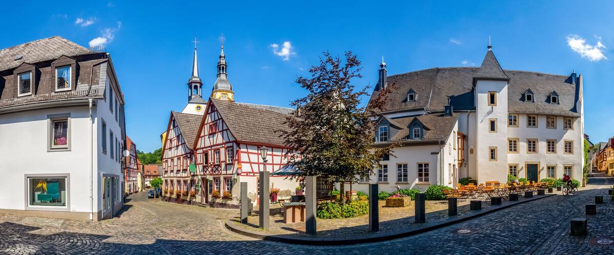A cobblestone street lined with traditional half-timbered houses and a church with a spire.