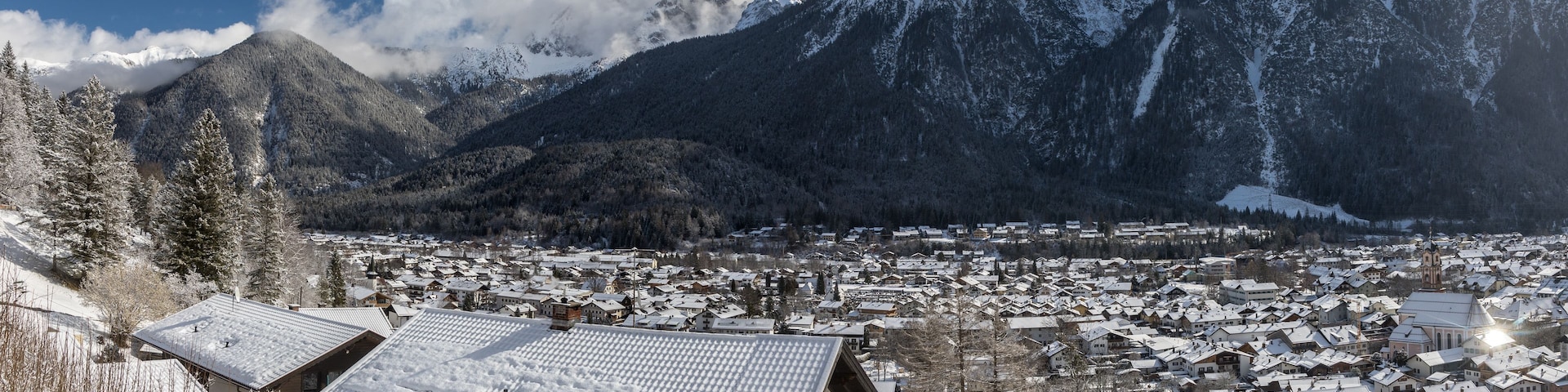 Un pueblo cubierto de nieve, enclavado entre montañas, con una imponente aguja de iglesia a la vista.