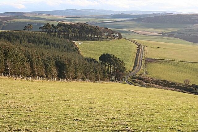 A rural landscape with rolling hills, a forested area, and a winding road.