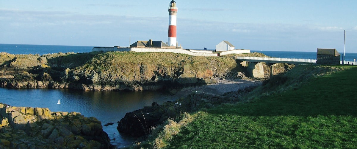 A lighthouse on a rocky outcrop with a bridge leading to a white building.