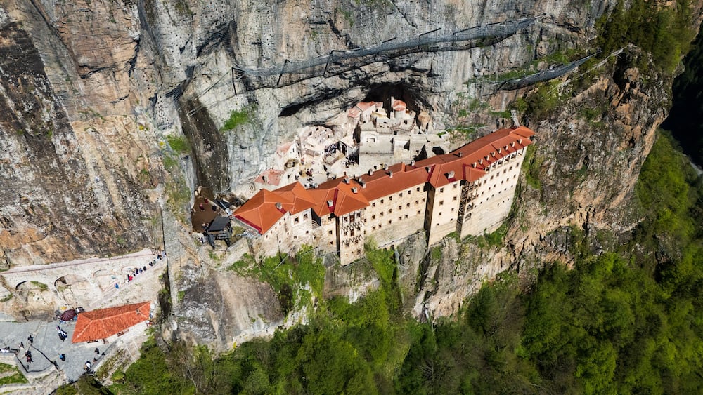 A monastery perched on a cliffside with a red-roofed building and a surrounding rocky landscape.