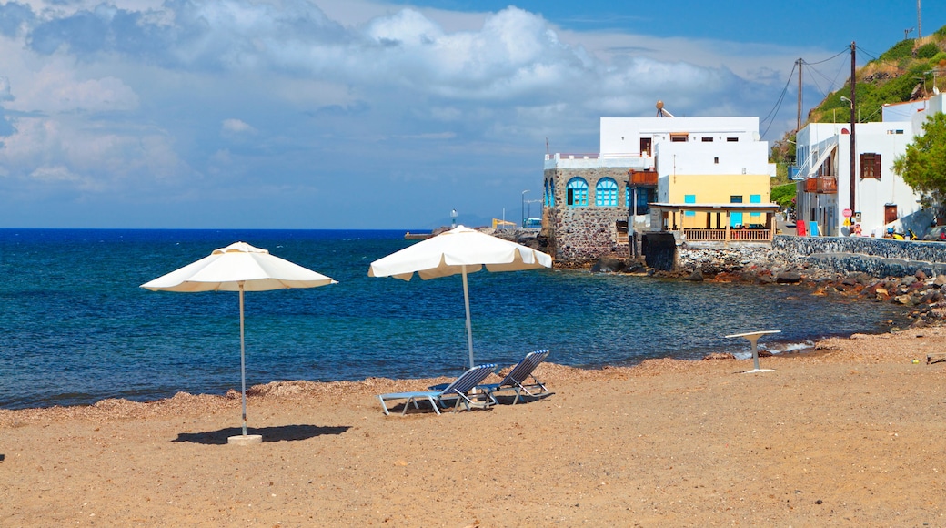 Une plage avec deux parasols blancs, une cĂŽte rocheuse et, en arriĂšre-plan, des bĂątiments aux couleurs vives.