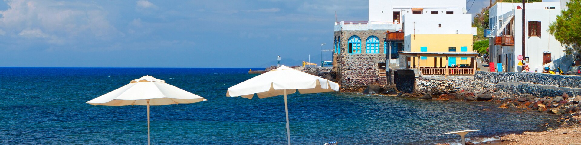 Una playa con dos sombrillas blancas, costa rocosa y edificios coloridos al fondo.