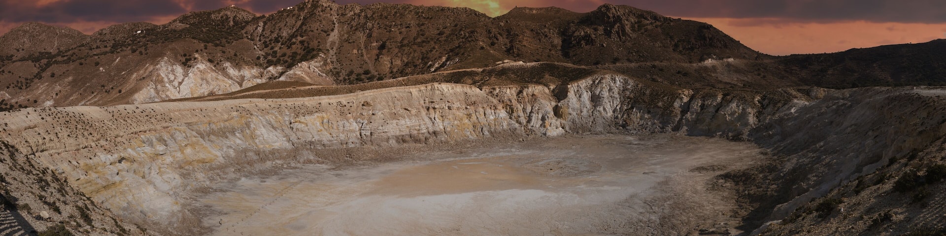 A barren landscape with a large crater surrounded by rocky hills.